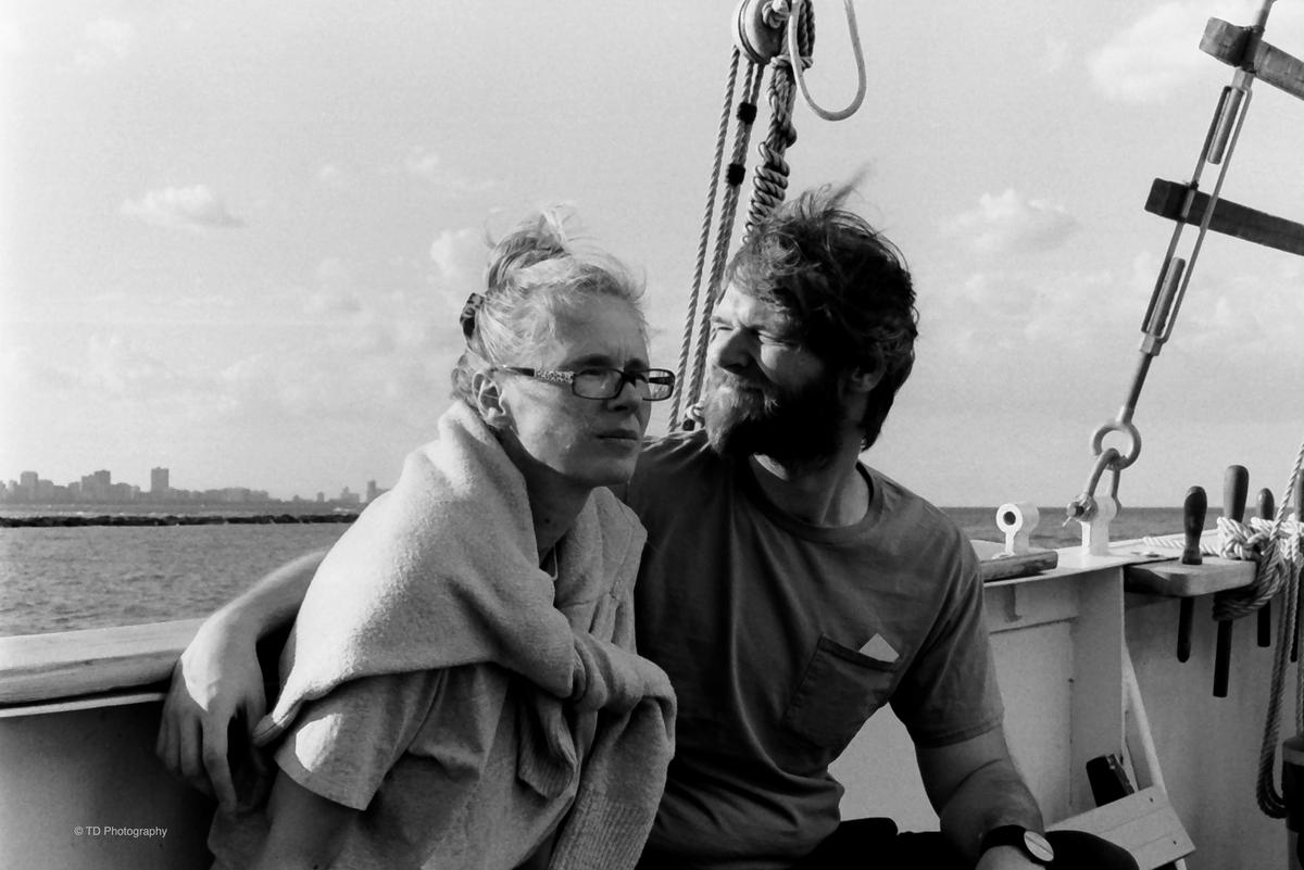 A couple sits on a boat with a city skyline in the distance.