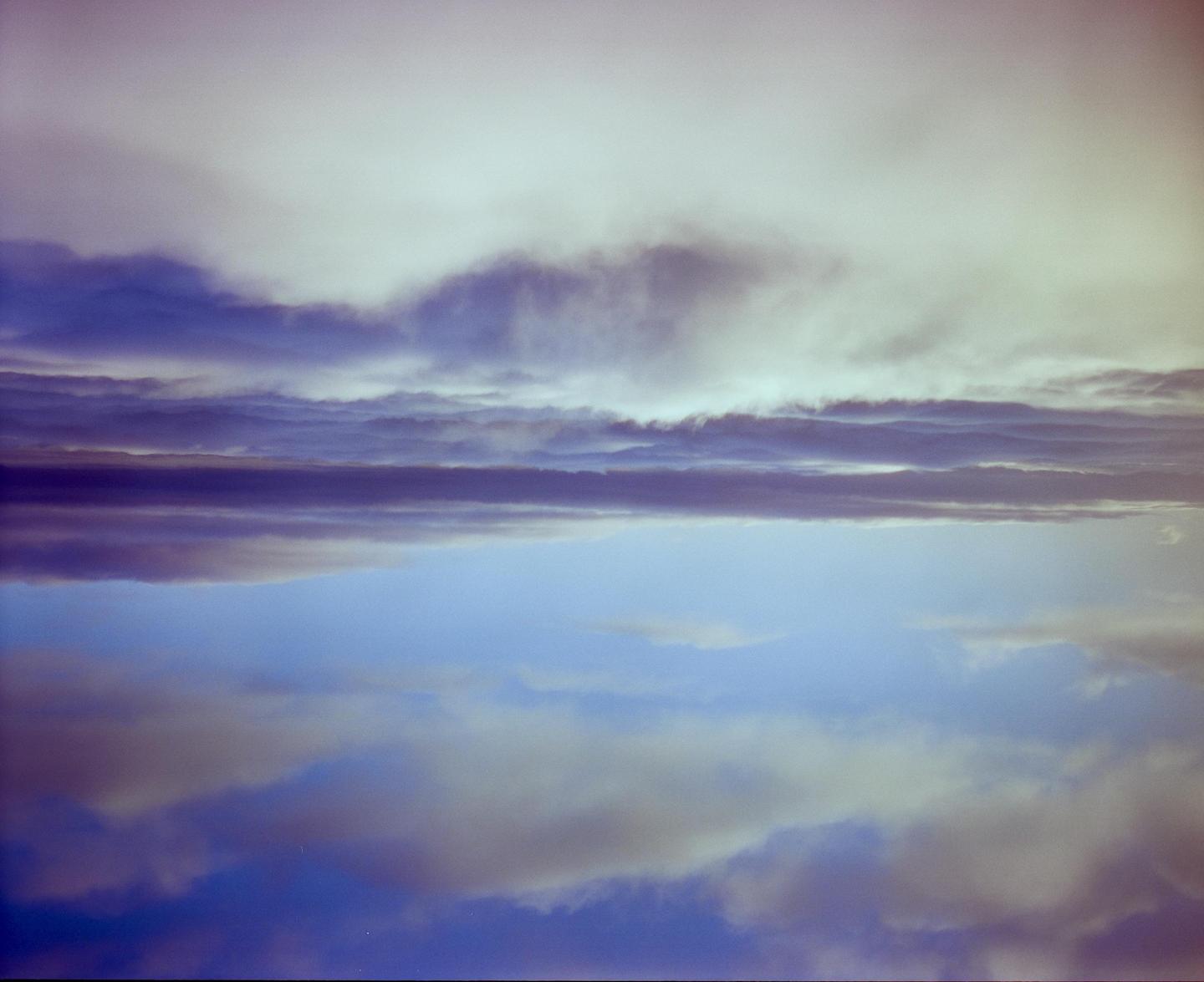 Clouds are reflected in a body of water, creating a symmetrical composition.
