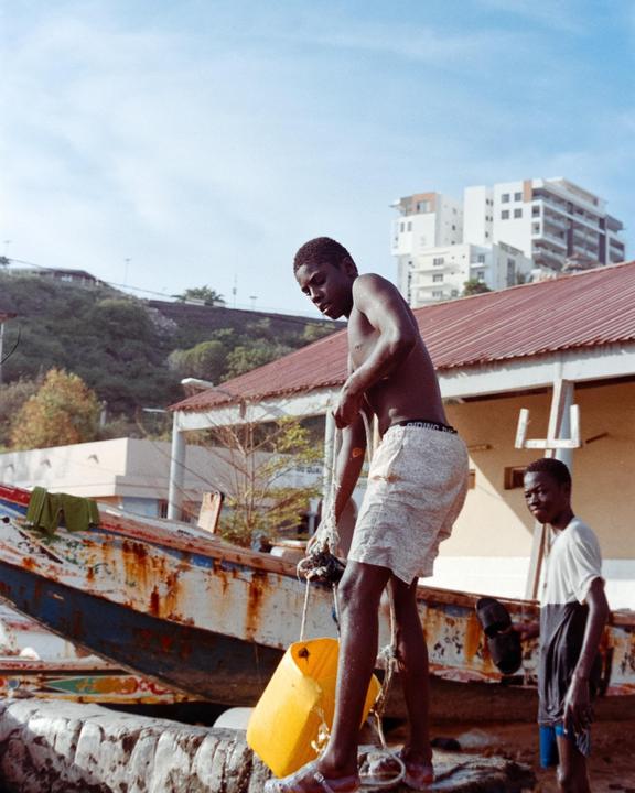 A boy stands on a boat and holds a yellow buoy while another boy stands behind him.
