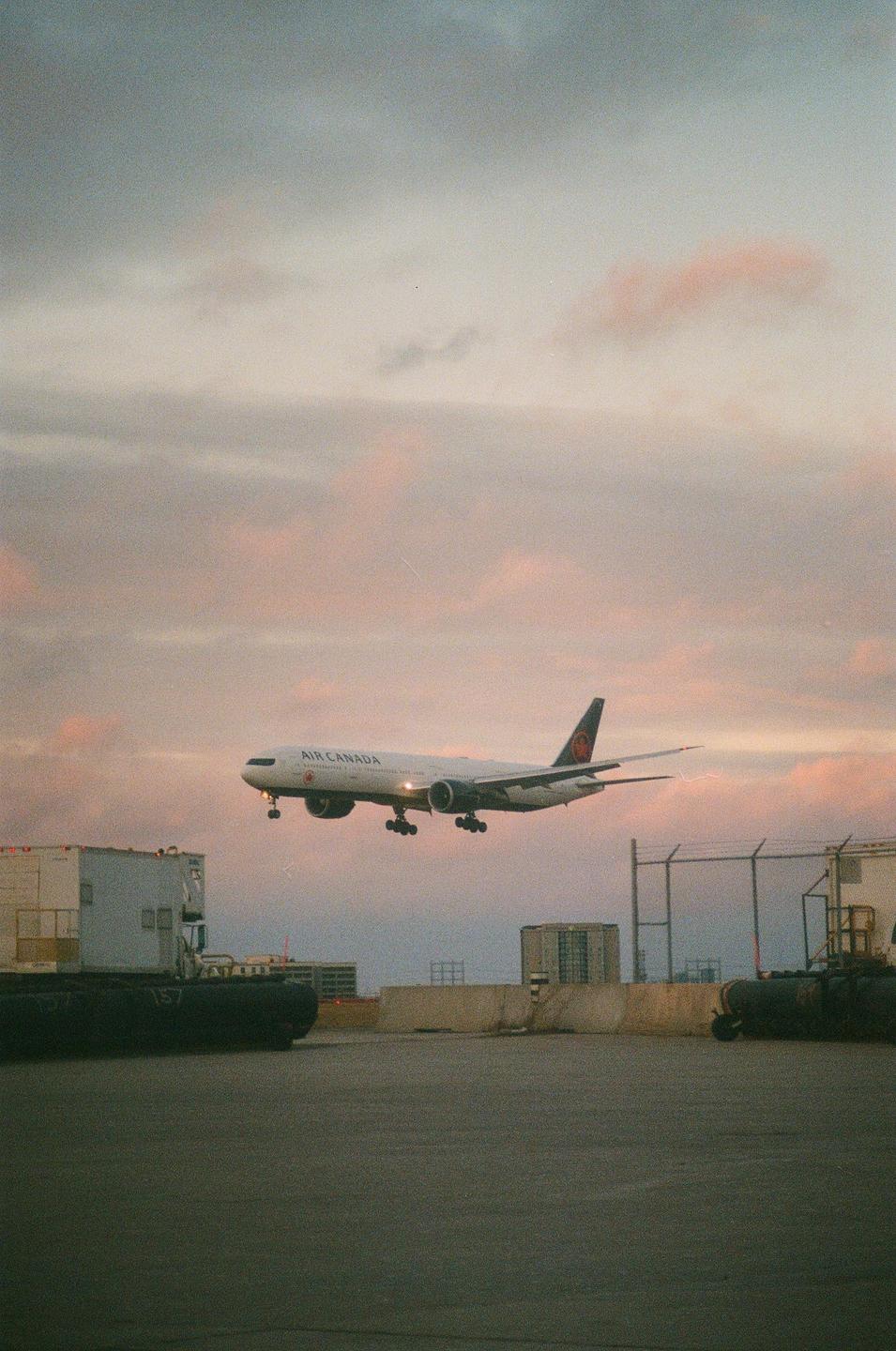 An Air Canada airplane descends for landing against a pastel sky.