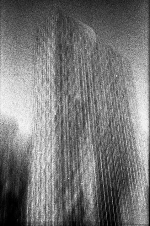 A blurry, grainy black and white image shows a tall, dark, textured structure with vertical lines.