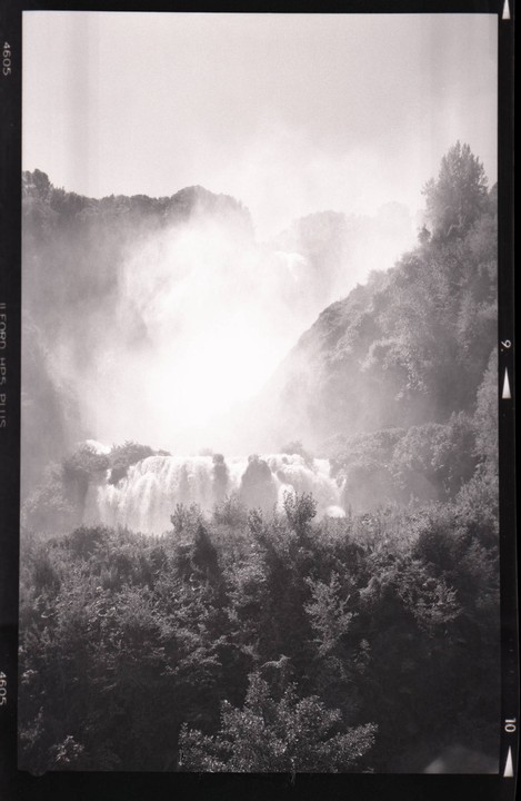 A large waterfall cascades down a rocky cliff surrounded by dense forest, with mist rising from the water.