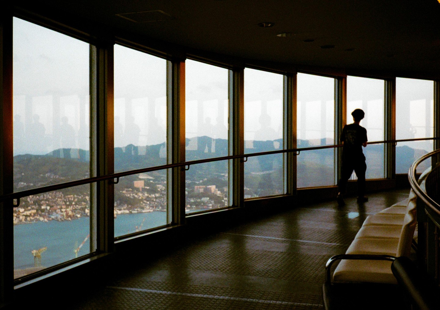 A person stands silhouetted against a large window overlooking a city and body of water.