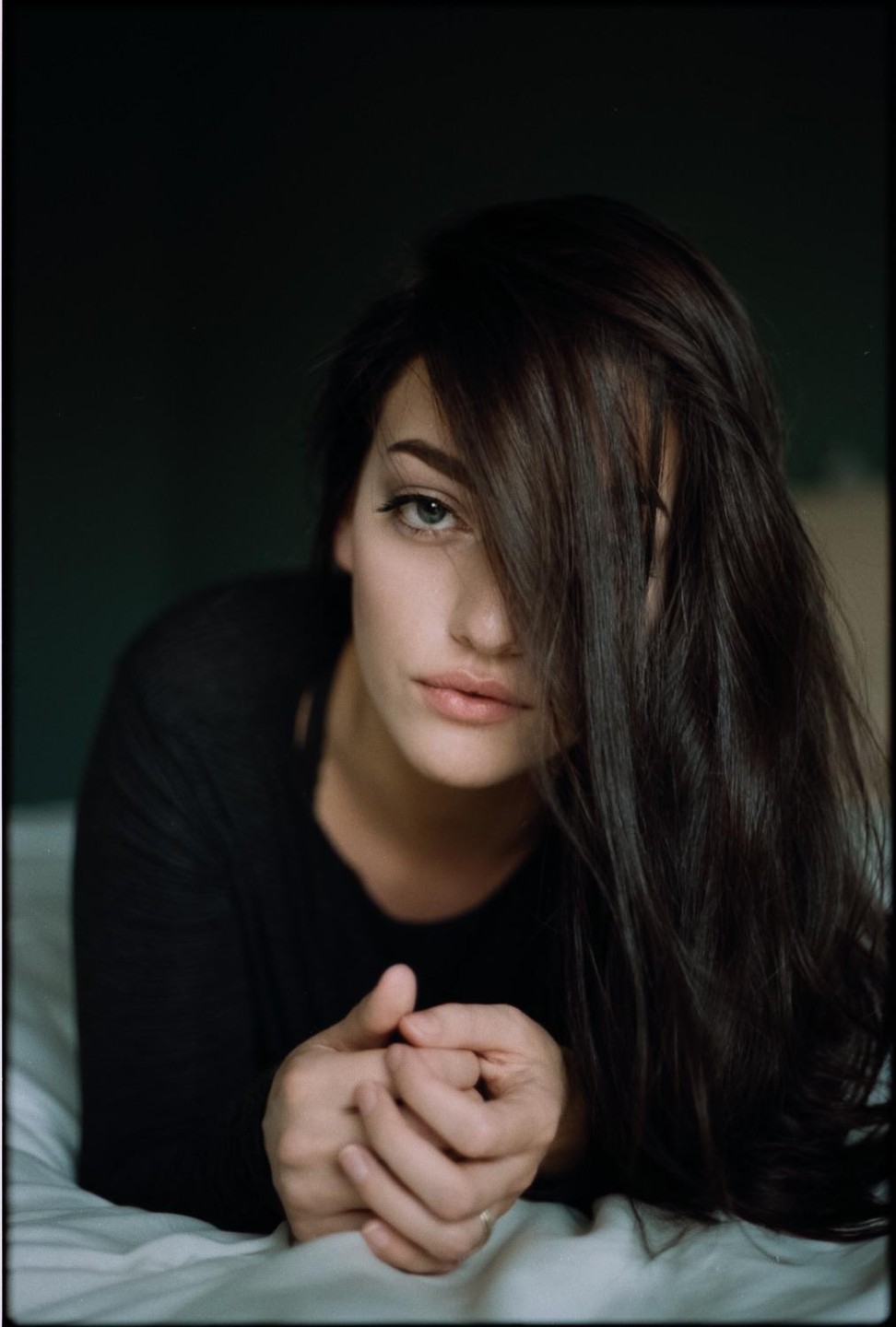 A woman with long dark hair covering part of her face lies on a bed.
