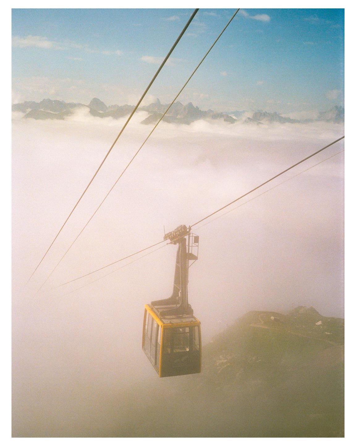 A yellow cable car travels through a hazy, mountainous landscape with clouds obscuring the view.