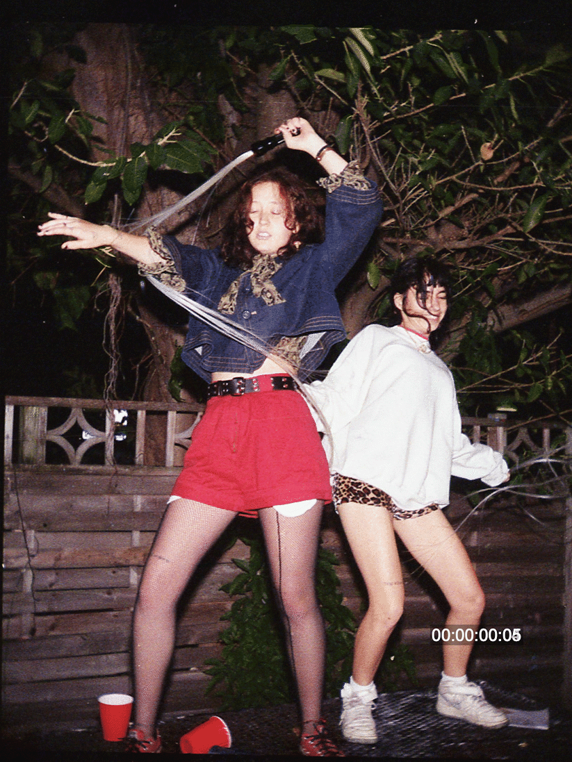 Two women dance at night, one holding a light-up whip and the other smiling.