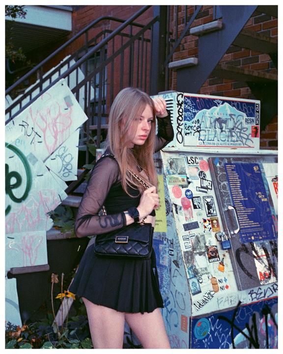 A woman stands on a street next to a metal staircase and a graffiti-covered utility box.