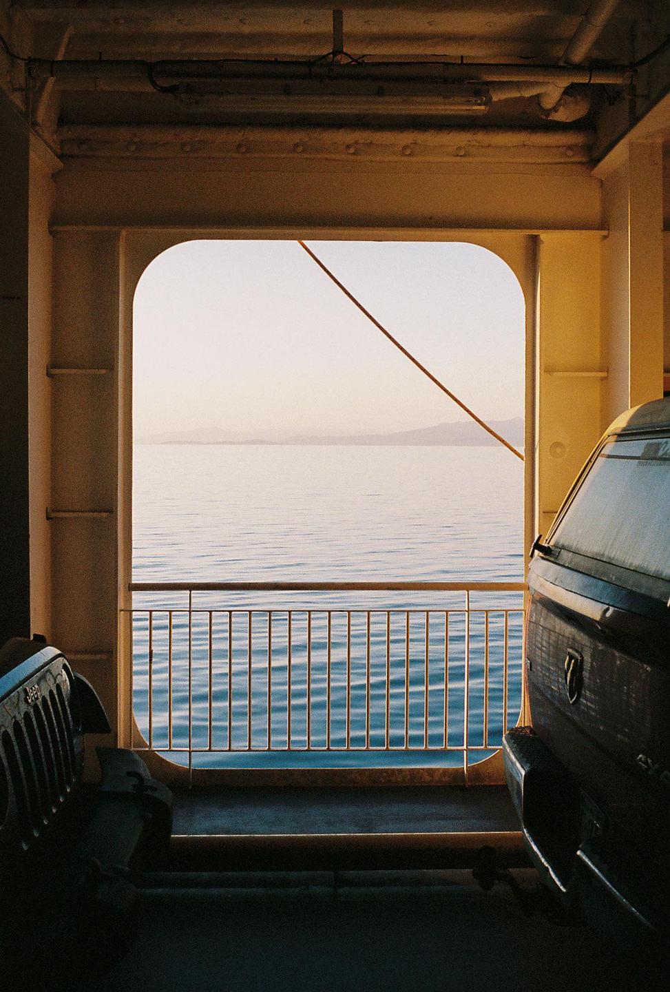 A view of the sea and distant mountains from inside a ferry with vehicles parked on deck.