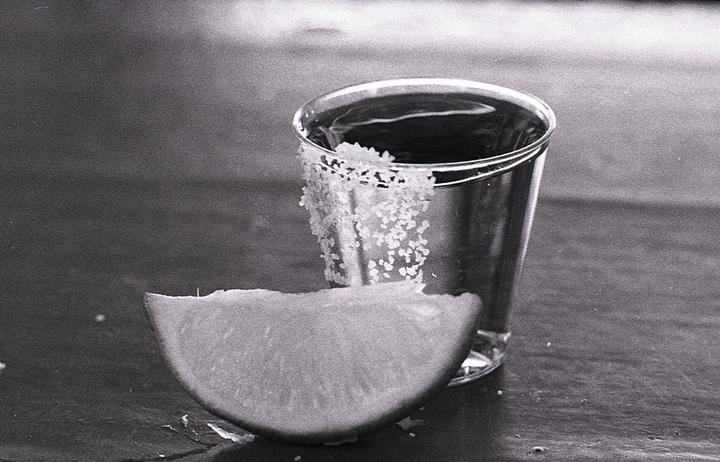 A shot glass with salt on the rim sits next to a lime wedge on a dark surface.