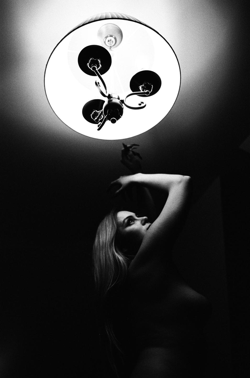 A woman looks up at a ceiling light fixture in a dark room.