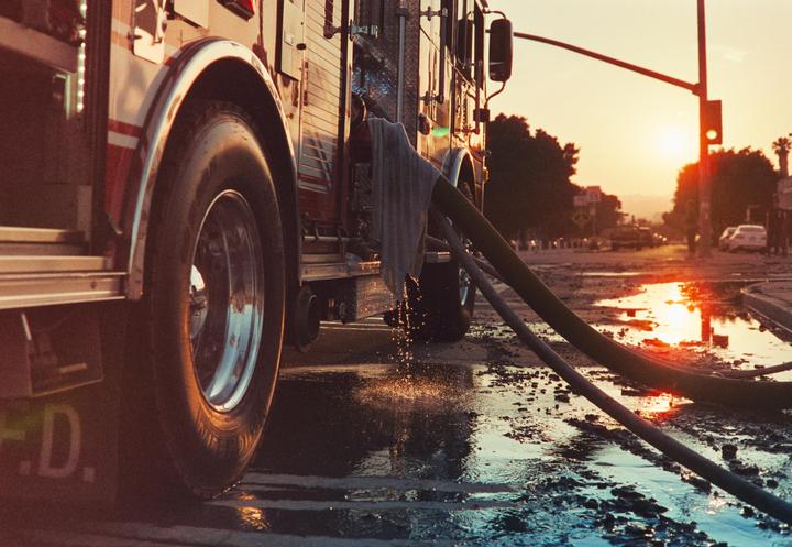 A fire truck is parked on a wet street with hoses on the ground and the sun setting in the distance.