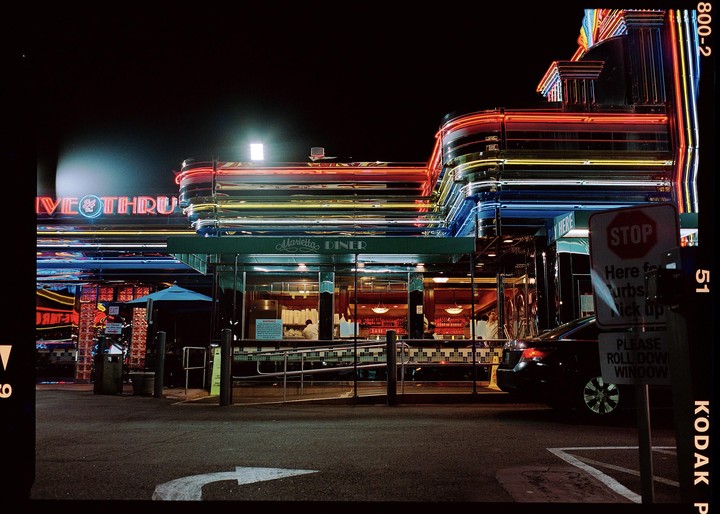 A diner with neon lights and a drive-thru is illuminated at night.