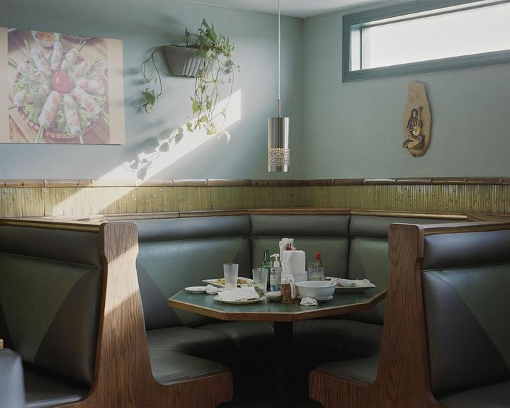 A restaurant booth with a table full of dirty dishes is illuminated by a shaft of sunlight.