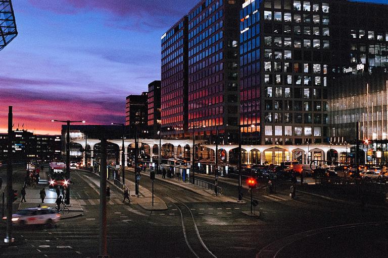 A city street at dusk shows buildings with illuminated windows and a colorful sky.