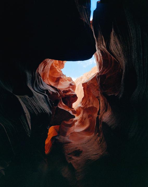 A narrow slot canyon with orange and red rock formations is illuminated by light from above.