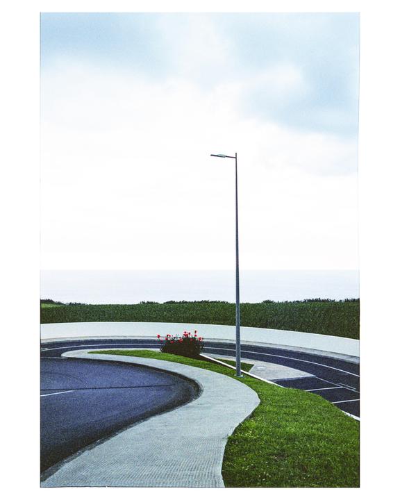 A curved road and sidewalk lead to a distant ocean under a cloudy sky.
