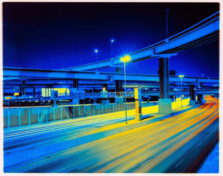 A highway interchange is illuminated at night with blue and yellow light trails from vehicles.