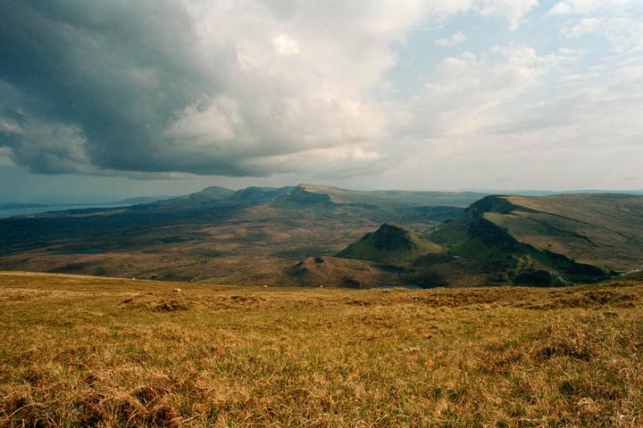 A vast landscape of rolling hills and mountains under a dramatic cloudy sky.