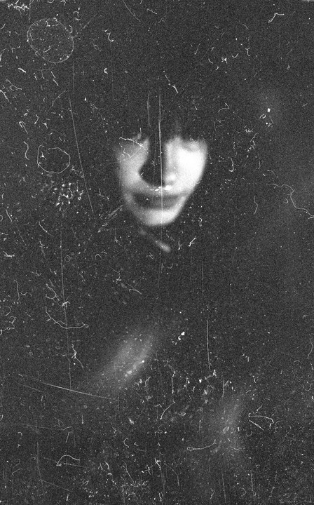 A blurry portrait of a woman with bangs is visible through a heavily scratched and dusty surface.
