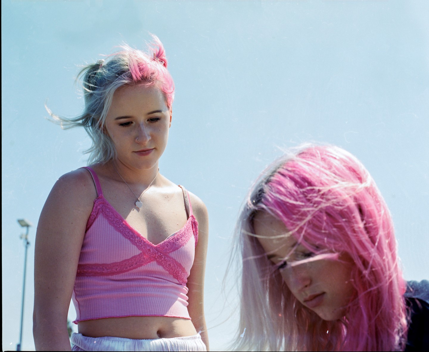 Two women with pink and blonde hair stand outside under a clear sky.