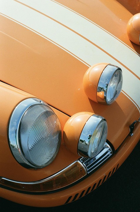 The front of an orange car with white racing stripes and four headlights is visible.