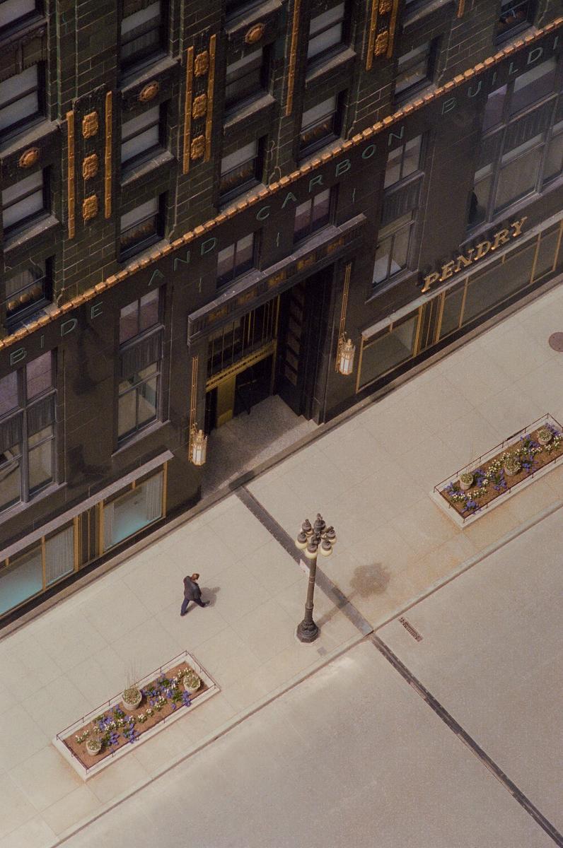 A man walks on a sidewalk next to a large building with ornate details and a street lamp.