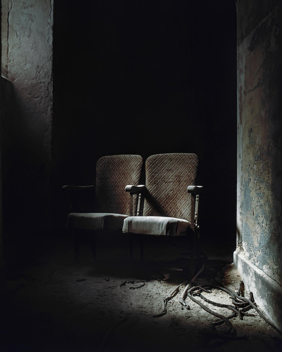 Two dusty, abandoned theater seats are illuminated by a shaft of light in a dark room.