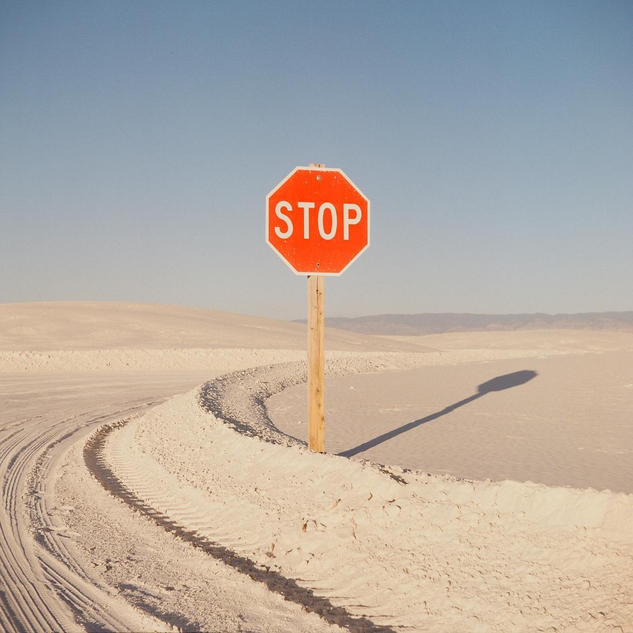 A stop sign stands in a desert landscape with tire tracks in the sand.