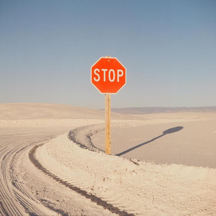 A stop sign stands in a desert landscape with tire tracks in the sand.