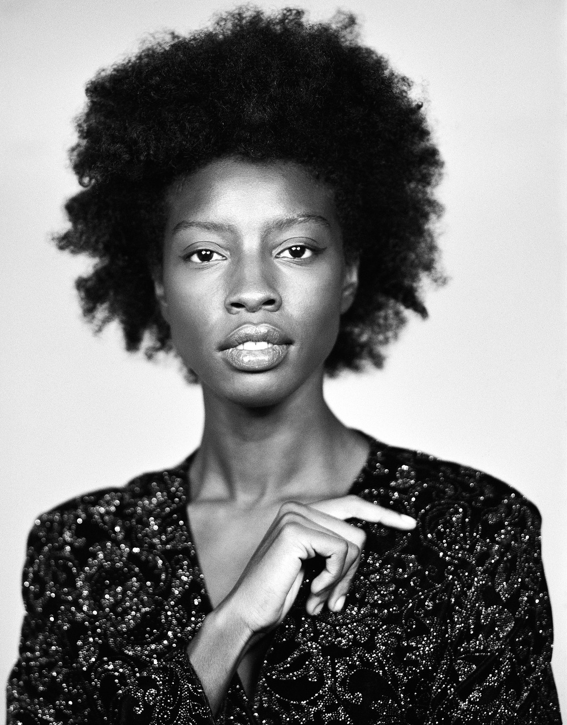 A woman with curly hair and a sequined top looks directly at the viewer.