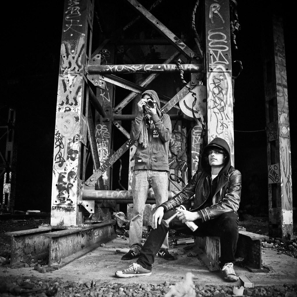 Two men stand and sit among graffiti-covered metal structures.