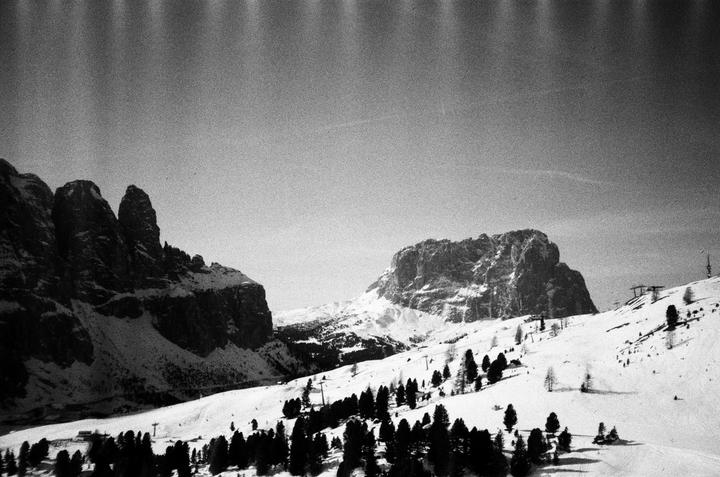 A black and white landscape shows a snow-covered mountain range with scattered trees and ski lifts.