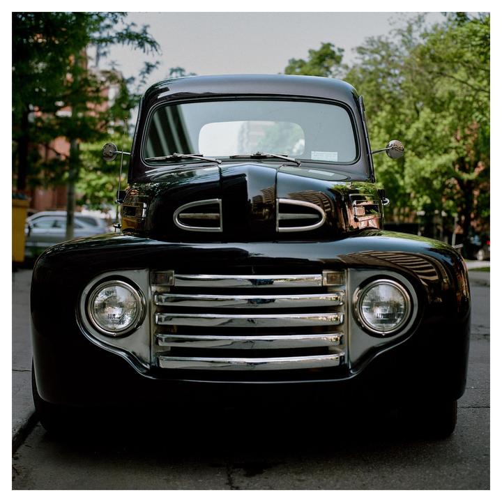 A black vintage truck is parked on a street lined with trees.