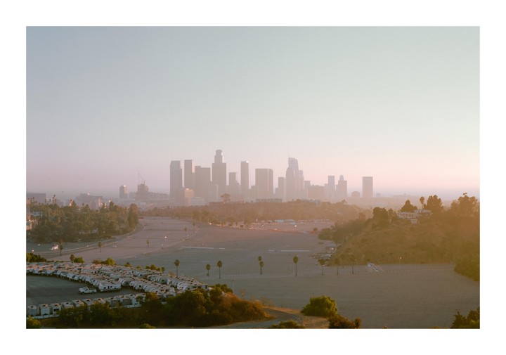 A hazy view of the Los Angeles skyline at dusk, with a large parking lot filled with recreational vehicles in the foreground.