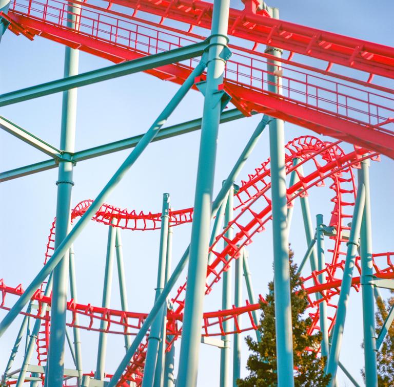 A red and blue roller coaster track twists against a clear sky.