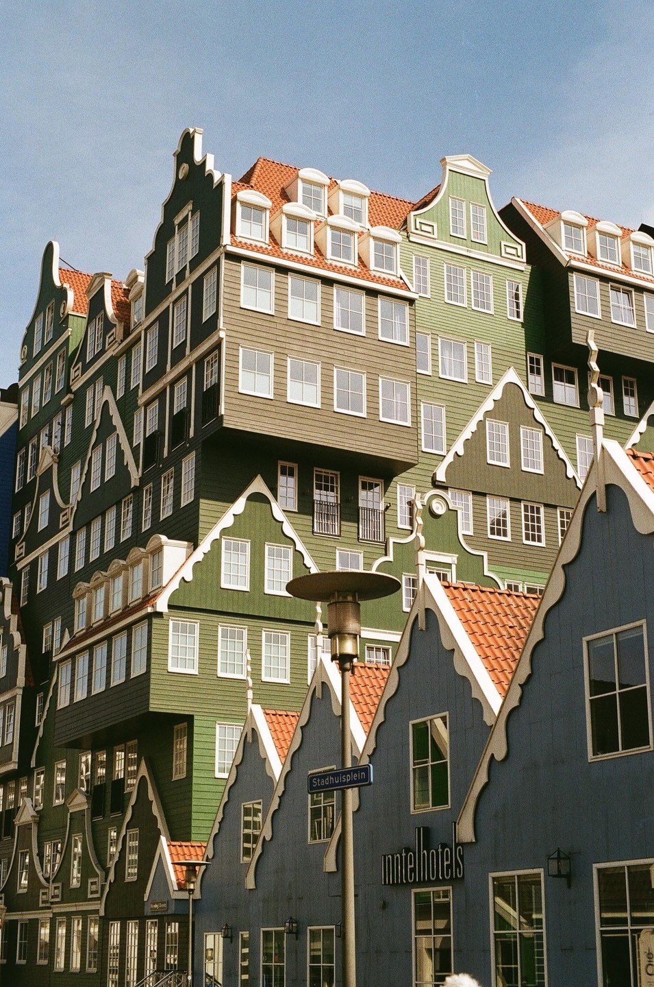 A cluster of buildings with traditional Dutch gables and red tile roofs are stacked together under a clear sky.