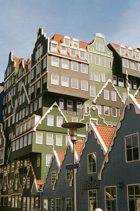 A cluster of buildings with traditional Dutch gables and red tile roofs are stacked together under a clear sky.