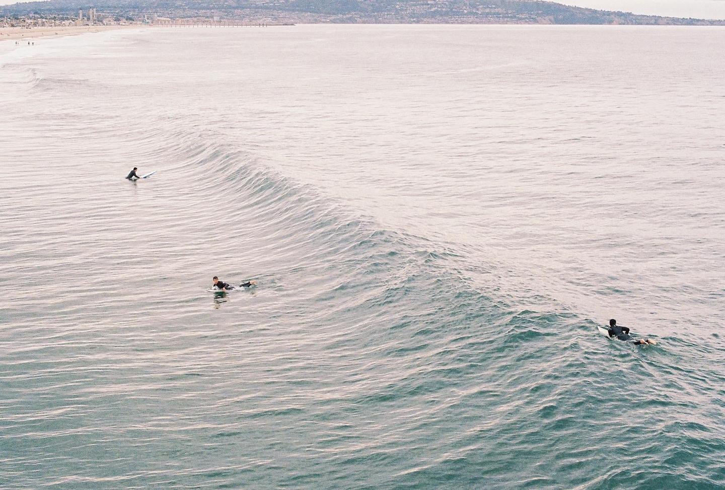 Three surfers are in the ocean with a large wave approaching the shore.