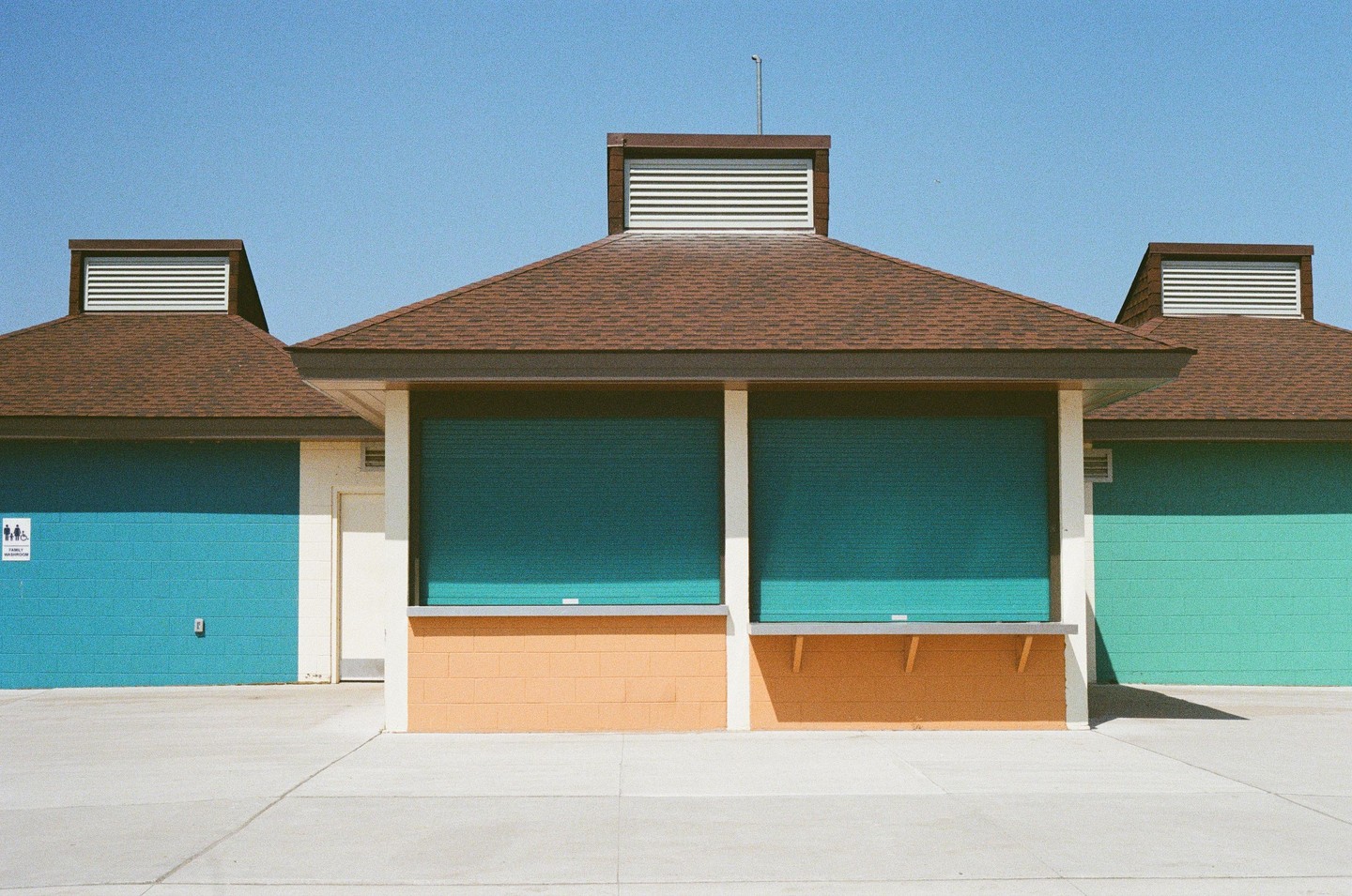 A snack shack with teal and orange walls stands under a clear blue sky.