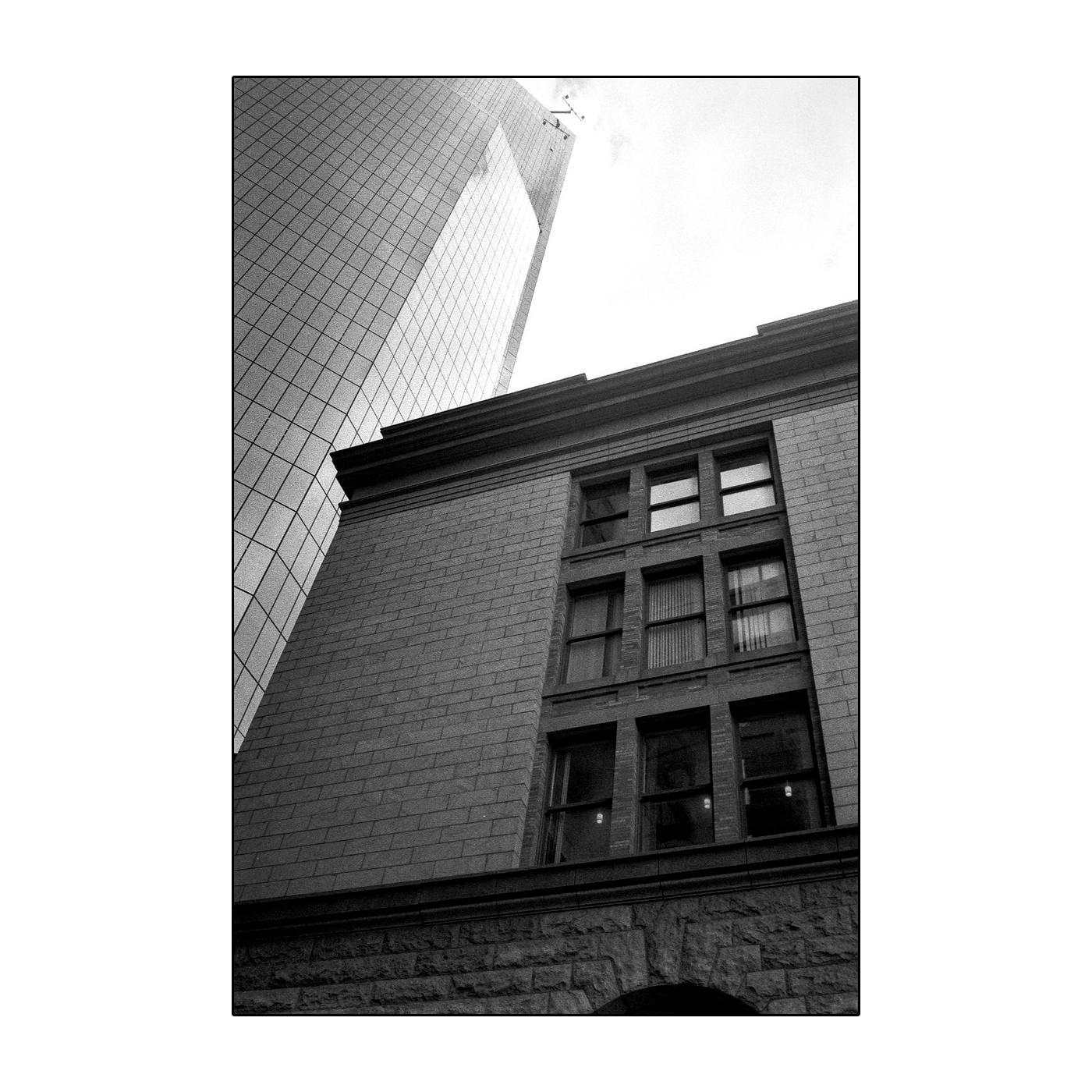 A tall, modern glass building stands behind an older brick building with many windows.