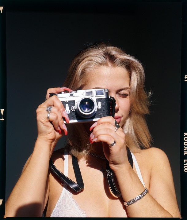 A woman holds a camera up to her face, obscuring her eyes.