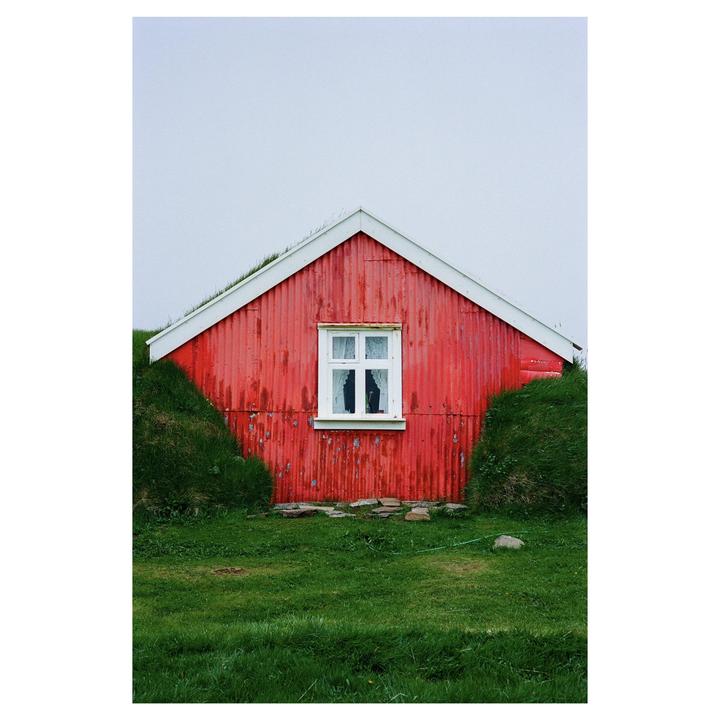 A red house with a white window is surrounded by green grass under a light sky.