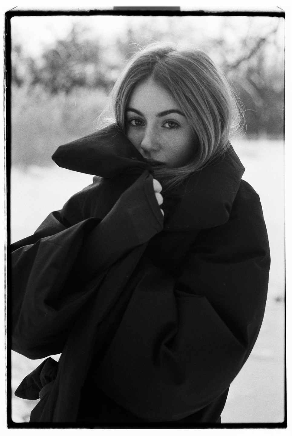 A woman in a large coat looks directly at the viewer.