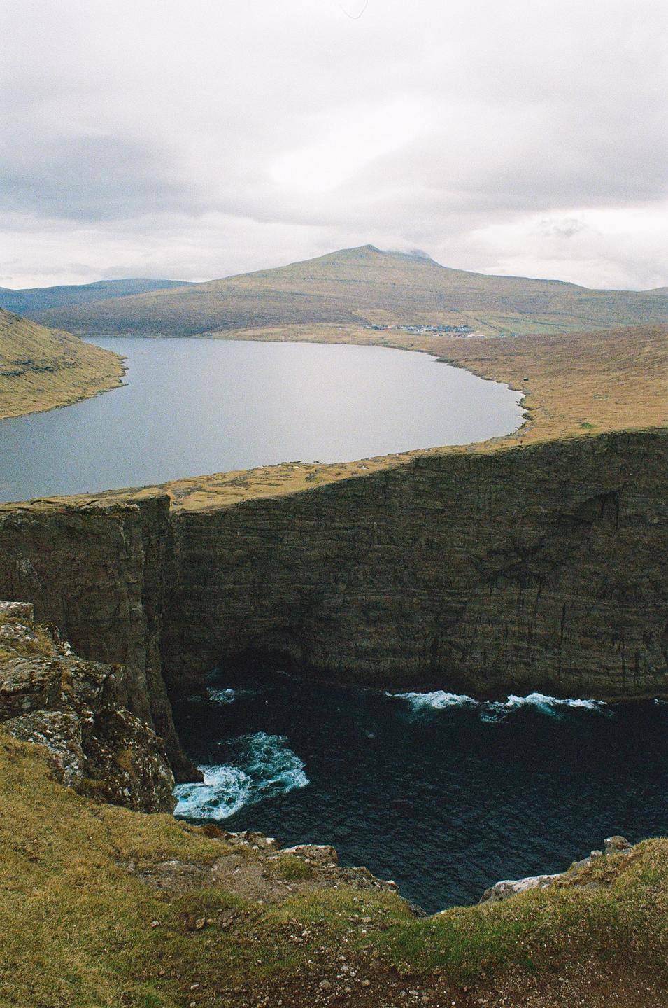 A large lake is visible behind a steep cliff face with ocean waves crashing below.