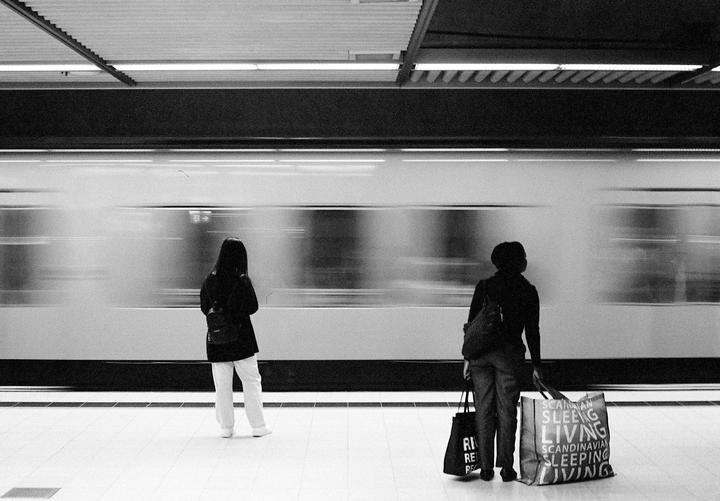 Two women stand on a subway platform as a train speeds by.
