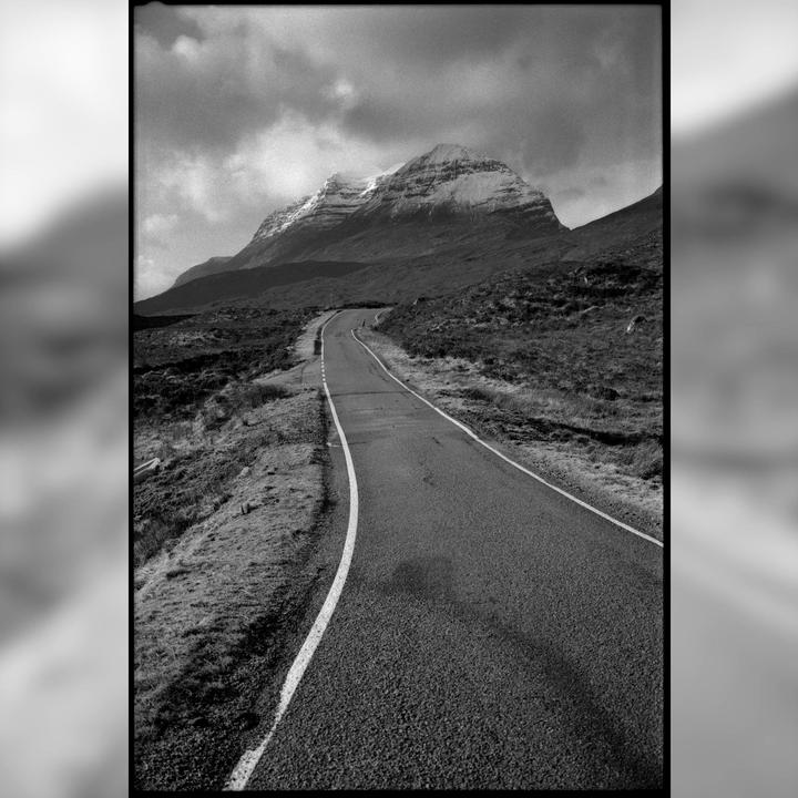 A winding road leads towards a snow-capped mountain under a cloudy sky.
