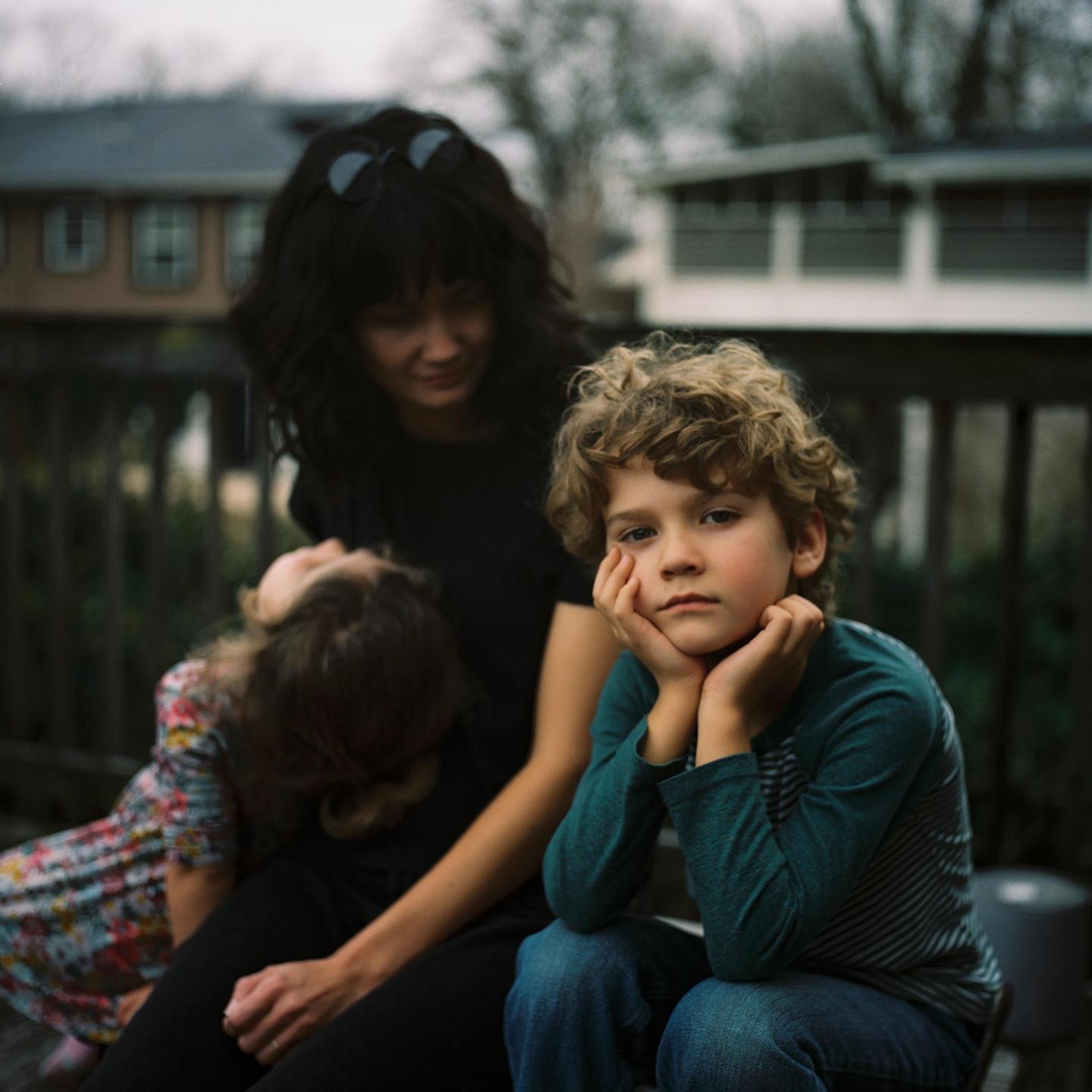 A woman and two children are sitting on a wooden deck outdoors.