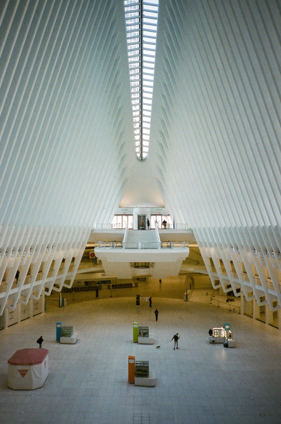 A large, bright, modern interior space with a high vaulted ceiling and a few people walking around.