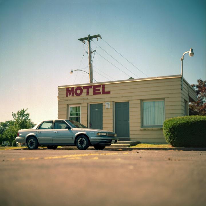 A silver car is parked in front of a motel with a "MOTEL" sign on its facade.