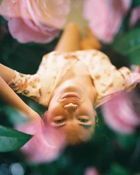 A woman with her head upside down is surrounded by pink flowers and green leaves.
